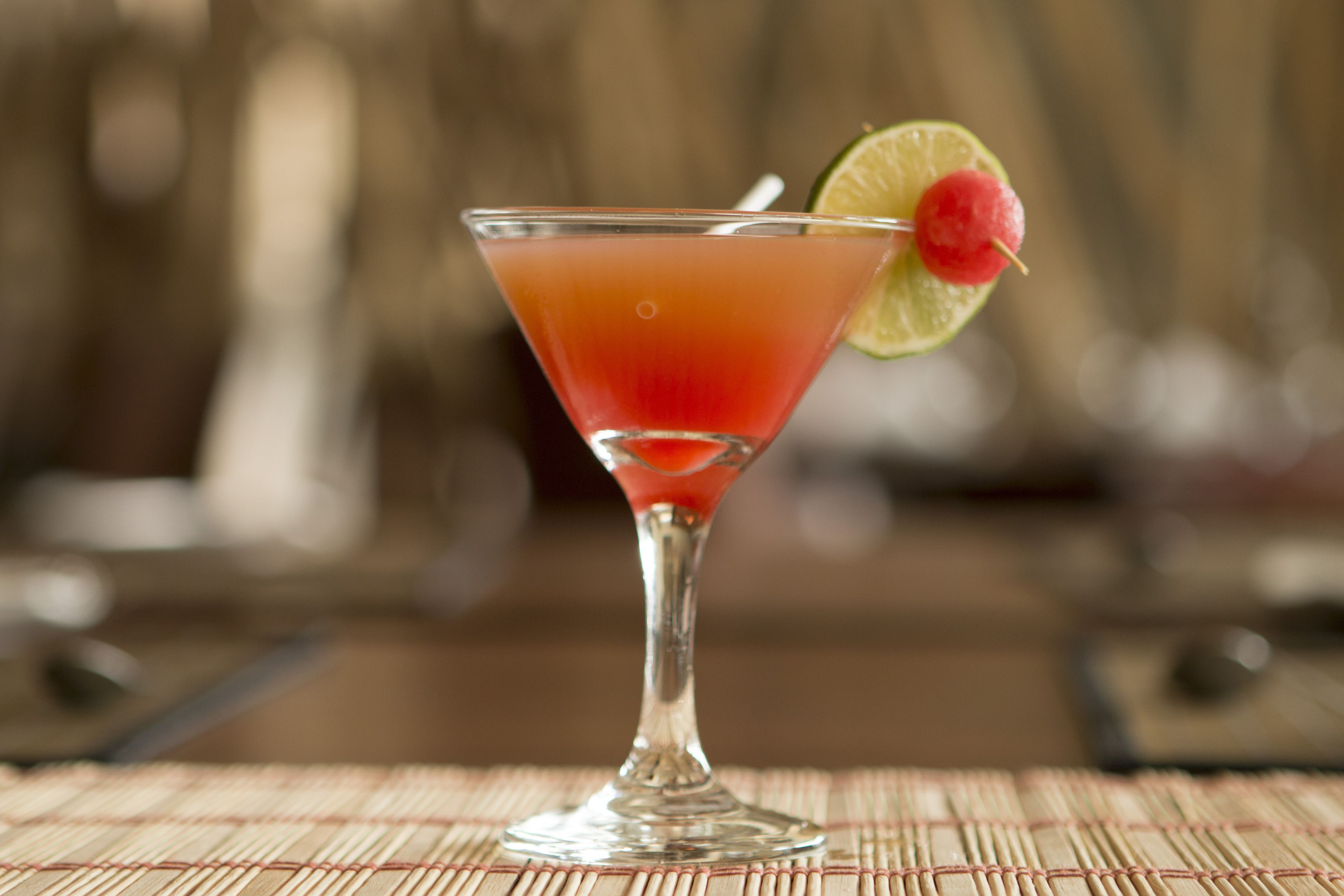 A cocktail in a martini glass with a lime wedge and a cherry on the rim.