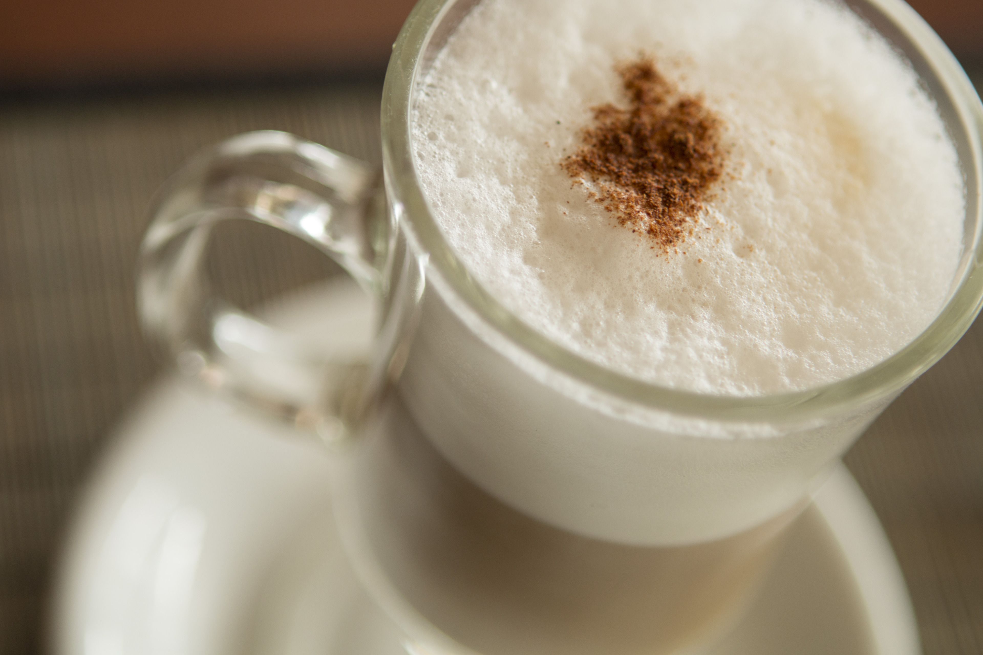 A clear glass cup with a frothy beverage and a sprinkle of spice on top.