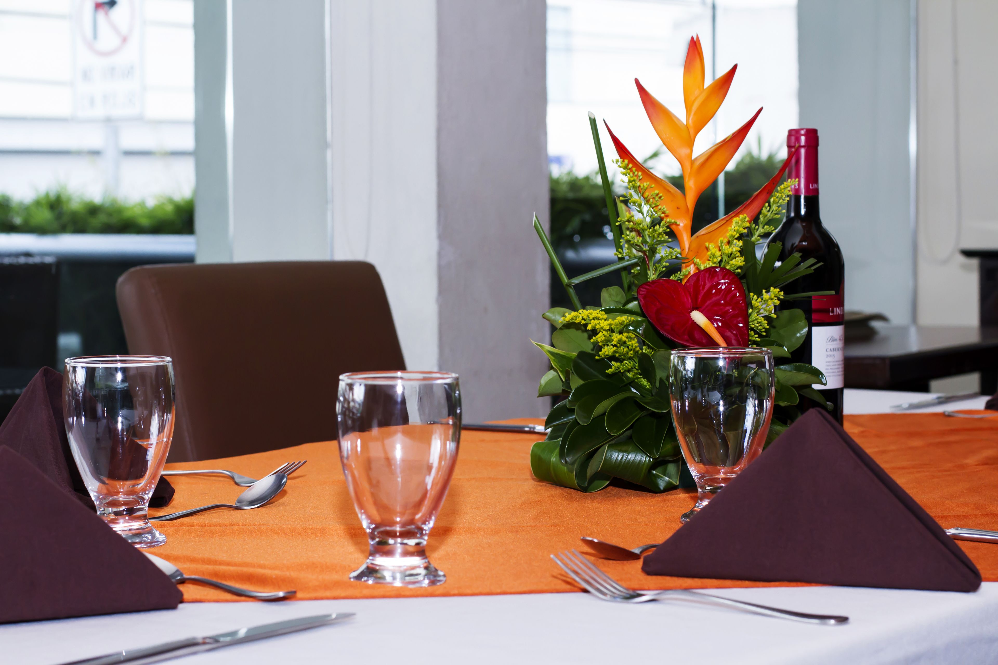 A dining table set with clear glasses, cutlery, and a decorative centerpiece with a bottle of wine.