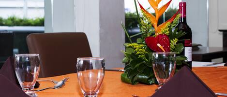 A dining table set with clear glasses, cutlery, and a decorative centerpiece with a bottle of wine.