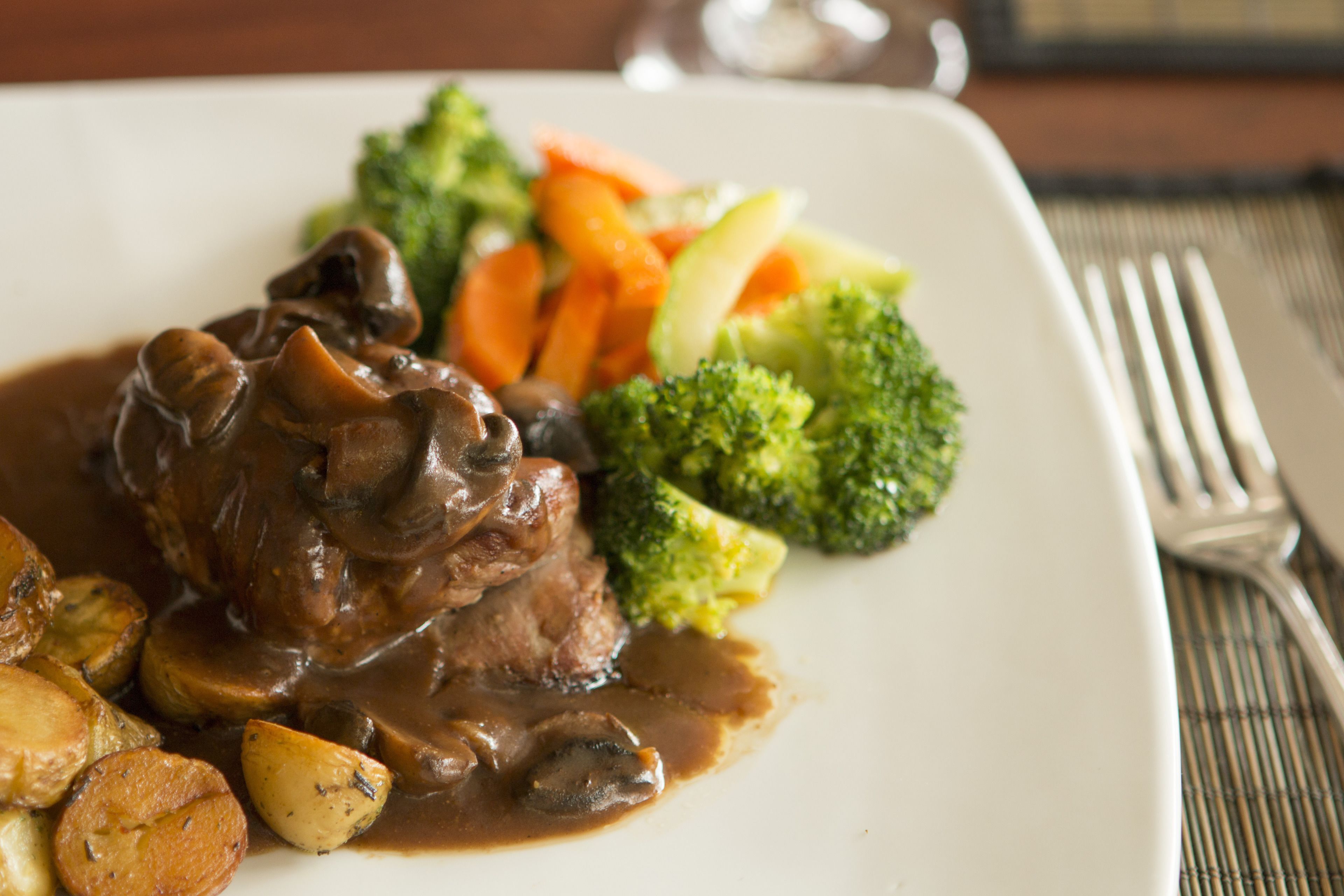 A plate of food with beef, mushrooms, carrots, and broccoli.