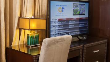 Ett hotellrum med en tv som visar en kanalguide för kabel-tv, ett glasbord med en dekorativ prydnad och en bekväm fåtölj.