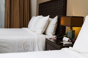 Una habitación de hotel con una cama, almohadas, una mesita de noche con lámpara, un teléfono y un cartel.