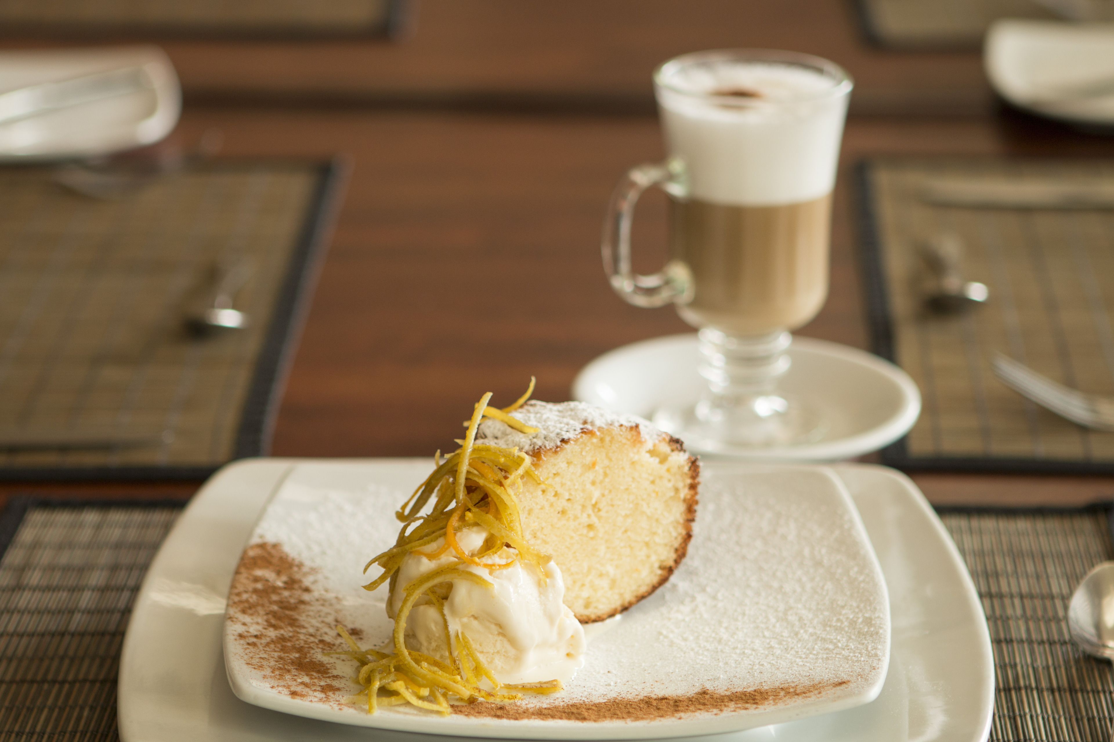 A dessert plate with a slice of cake, a scoop of ice cream, and lemon zest on a white plate.
