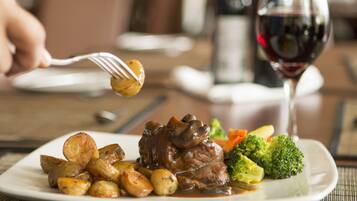 A plate of food with a fork lifting a piece of meat, a glass of red wine, and a bottle of wine in the background.