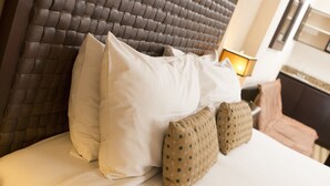 Una cama con cabecera capitonada, ropa de cama blanca y dos almohadas estampadas.