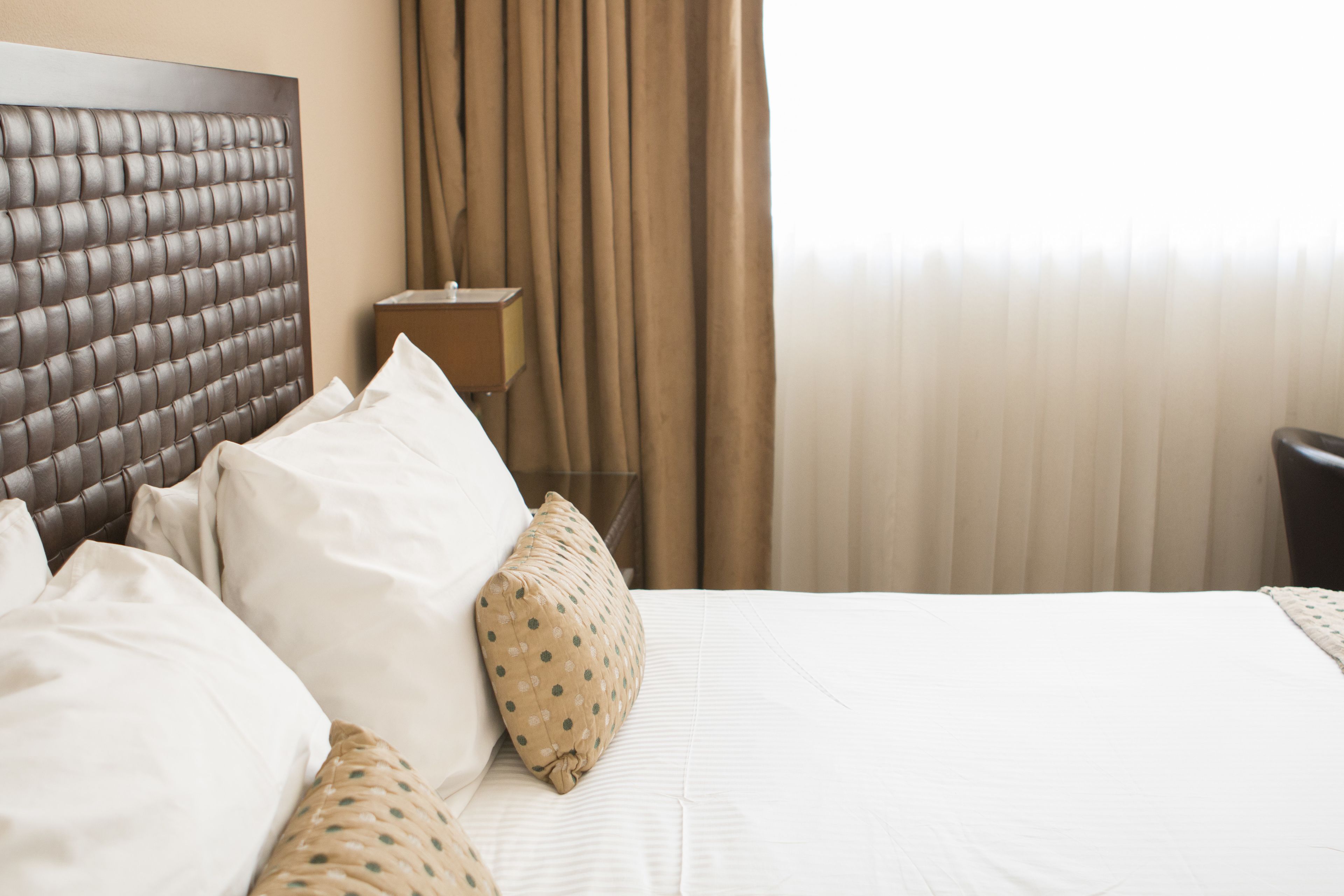 A neatly made bed with a headboard, a bedside table, and a lamp.