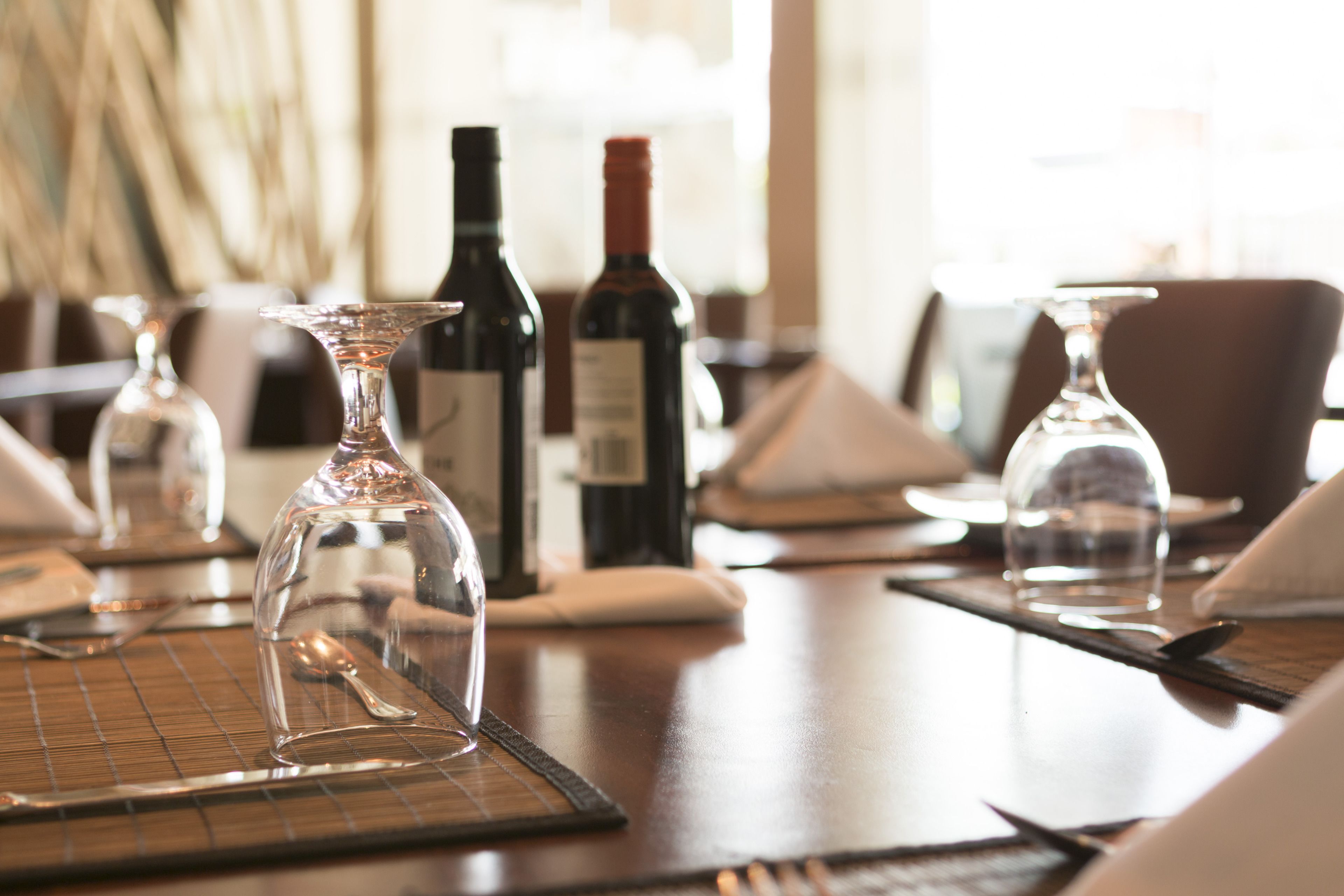 A dining table with wine bottles and glasses, set with placemats and cutlery.