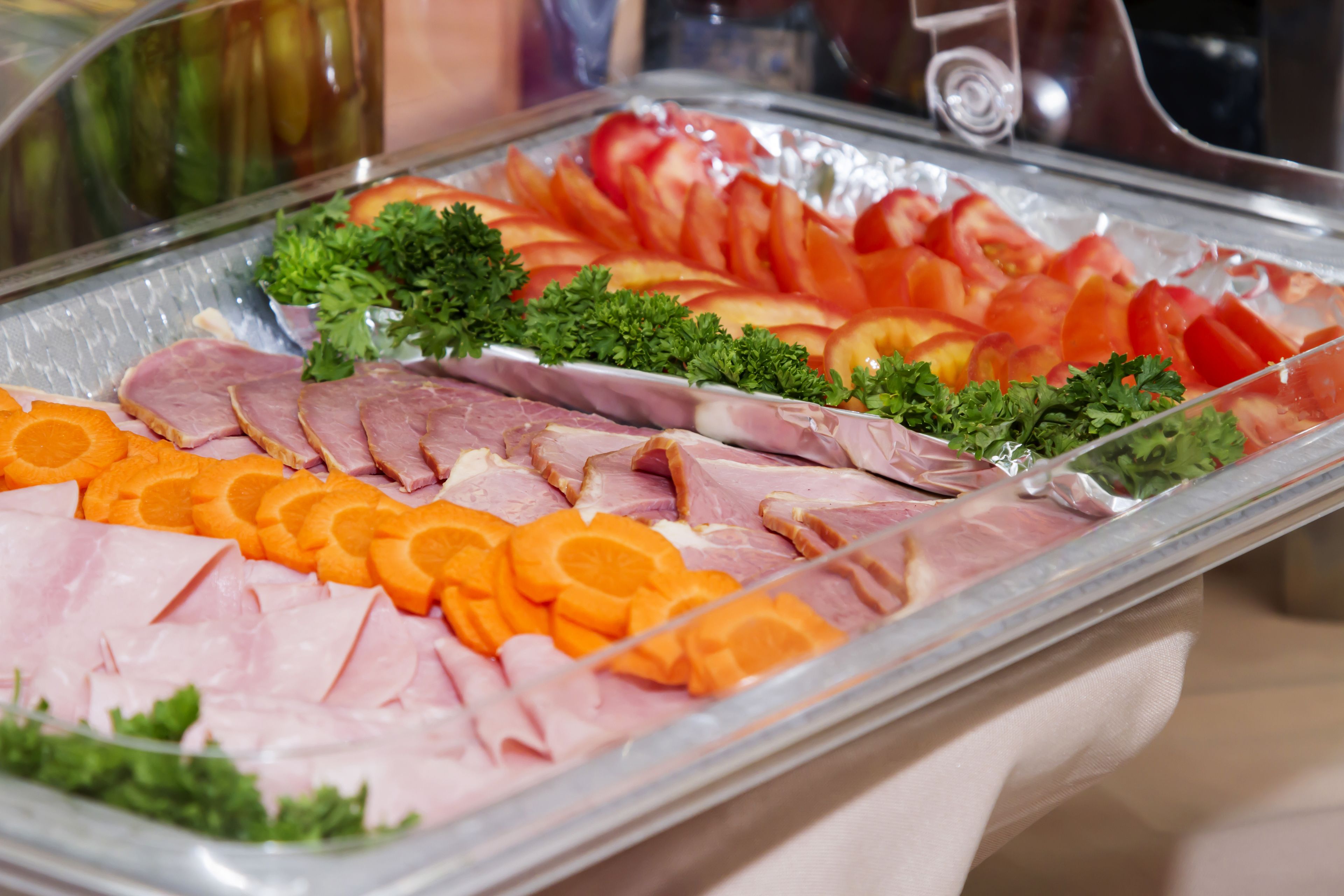 A buffet with sliced ham, oranges, tomatoes, and parsley.
