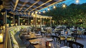 Un espace de restauration en plein air avec des tables et des chaises, un grand banc rembourré et des guirlandes lumineuses.