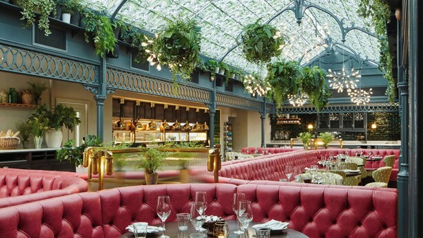 Un restaurant avec des banquettes rouges, un bar et un plafond en forme de serre, orné de plantes.