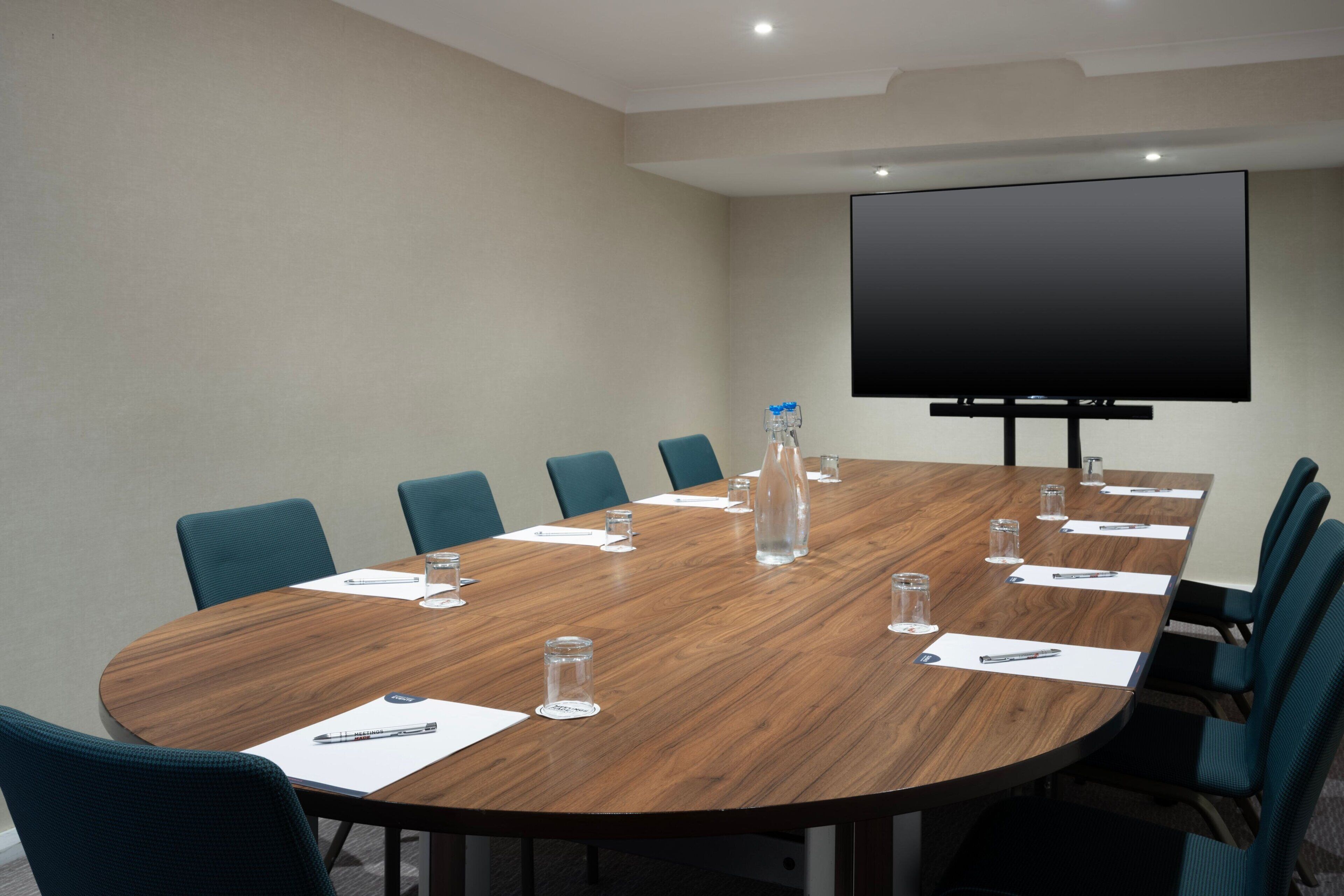 A conference room with a wooden table, blue chairs, a large screen, and water bottles.