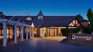 Un bâtiment de la chaîne Delta Hotels Marriott, pris au crépuscule, avec une façade en briques, une grande entrée vitrée et un espace extérieur couvert doté de colonnes.