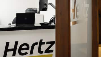 A desk with a laptop, a monitor, and a keyboard, with the word "Hertz" on the wall behind it.