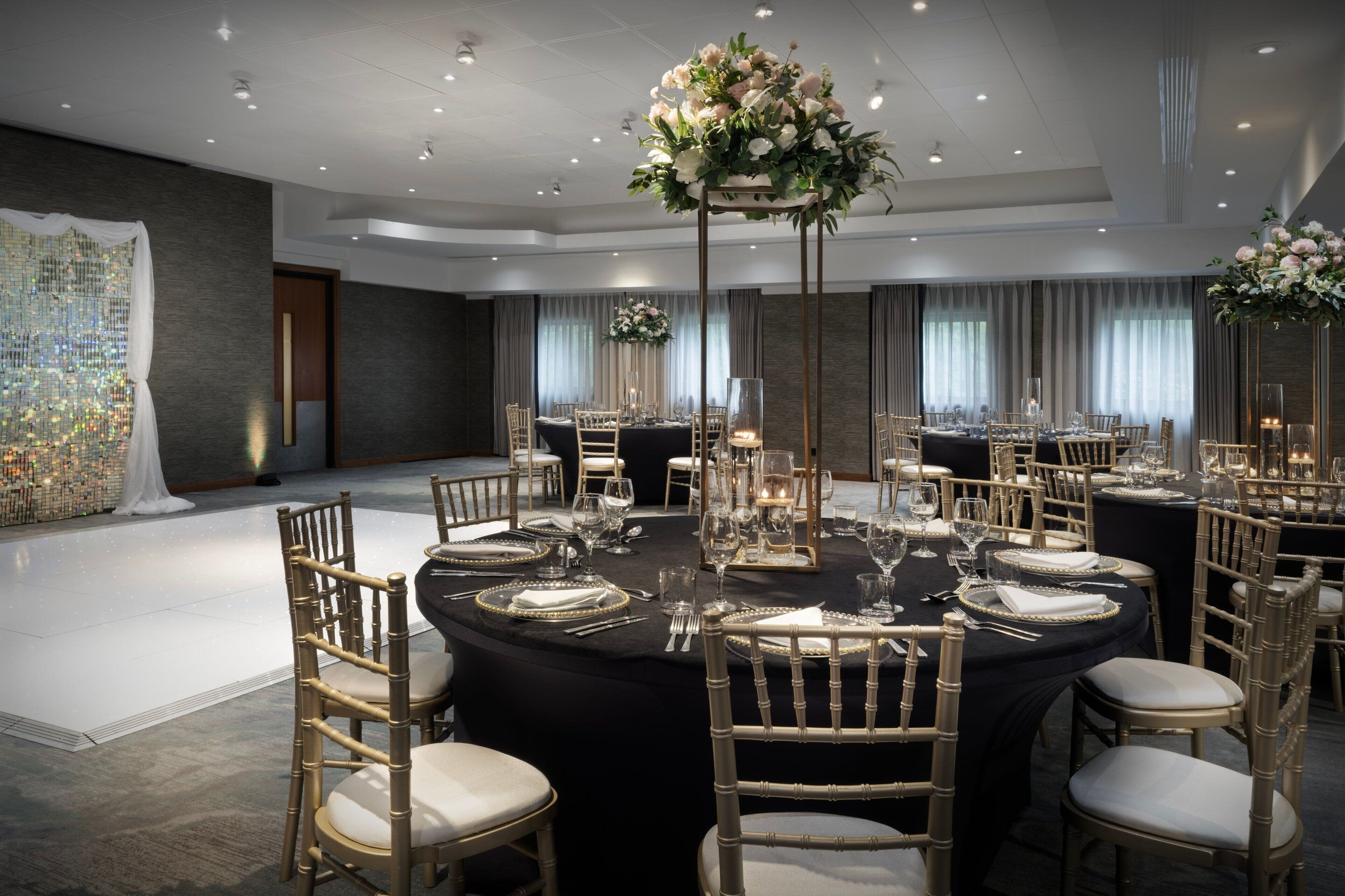 A banquet hall with round tables, gold chairs, and floral centerpieces.