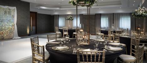A banquet hall with round tables, gold chairs, and floral centerpieces.