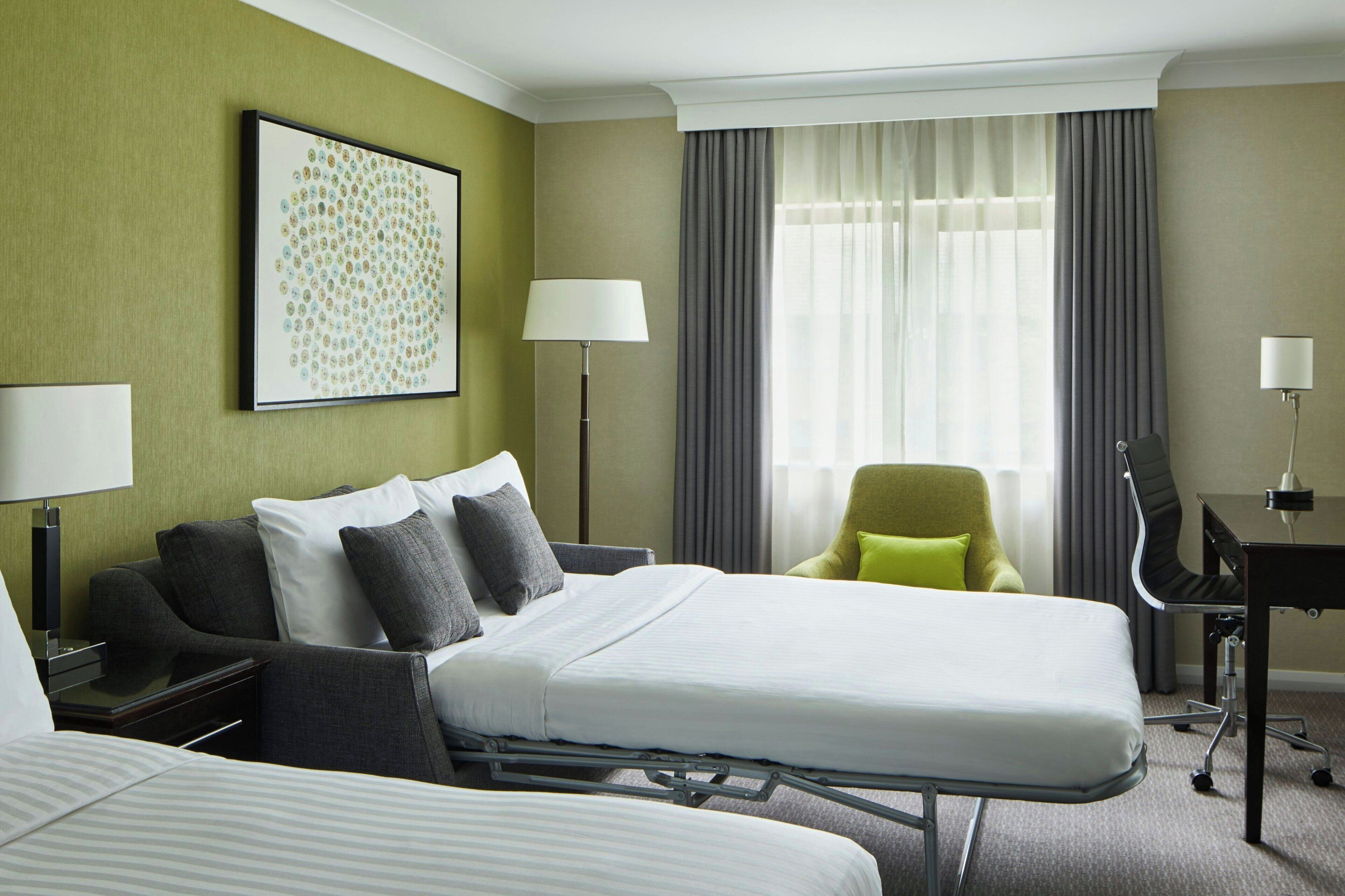 Quarto de hotel com uma cama grande, uma escrivaninha, uma cadeira e um abajur.