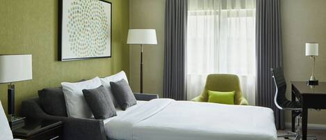 A hotel room with a large bed, a desk, a chair, and a lamp.
