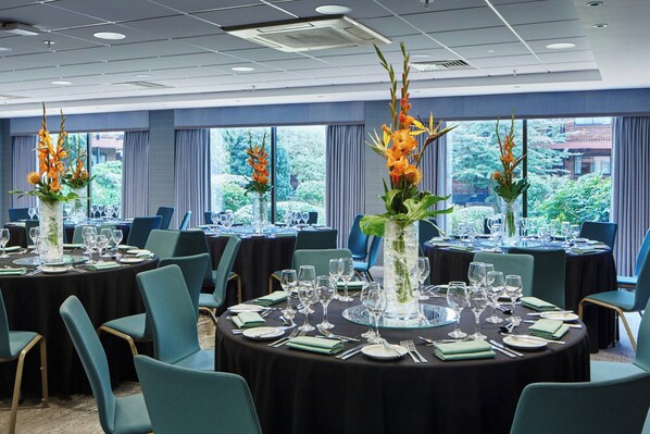 A conference room with round tables, teal chairs, and floral centerpieces.