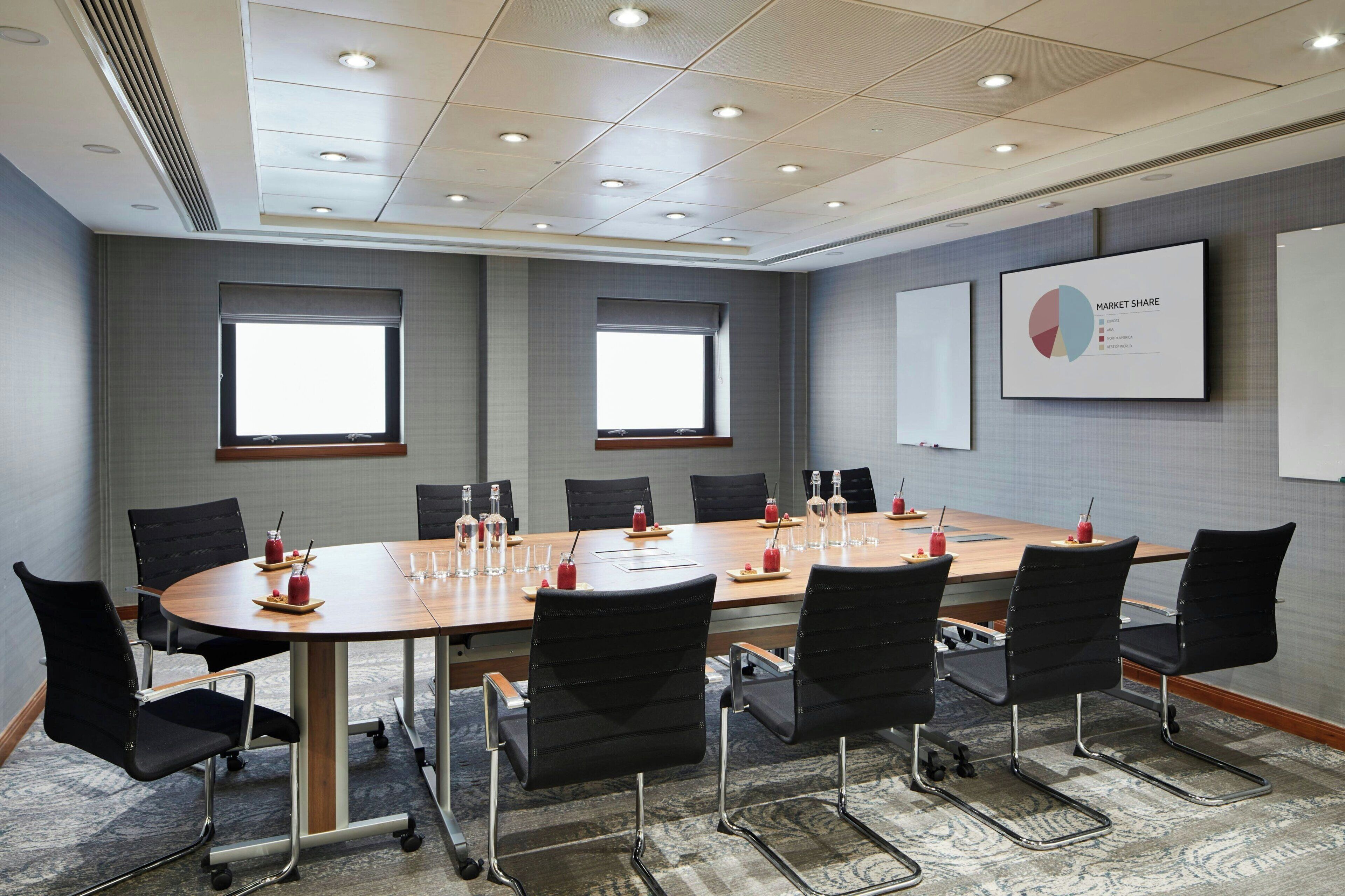 A conference room with a long table, black chairs, and a projector screen displaying a market share chart.
