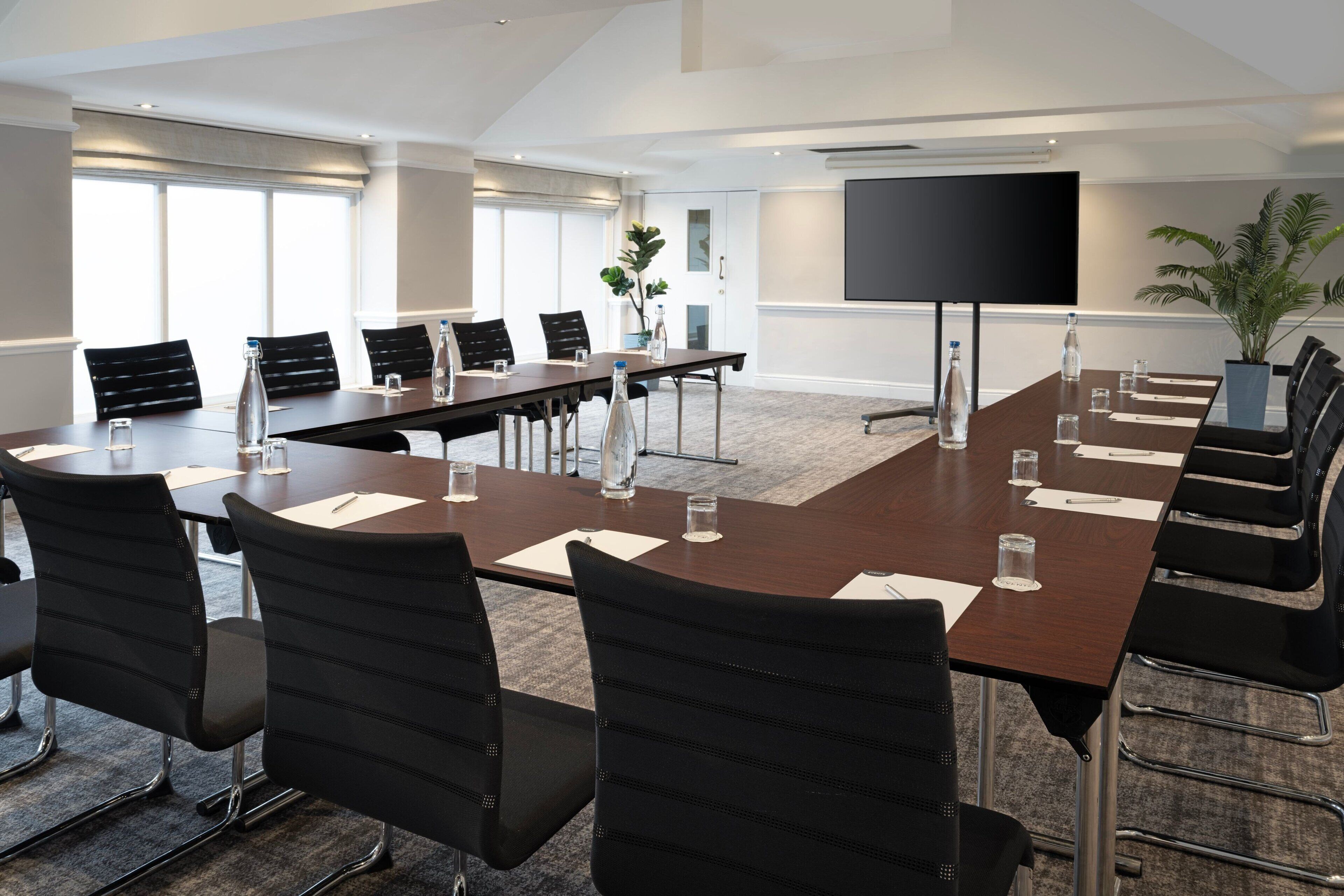 A conference room with a long table, black chairs, water bottles, and a large screen.