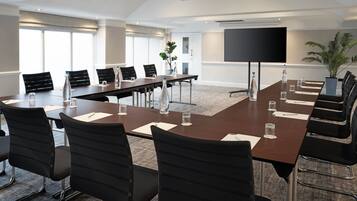 A conference room with a long table, black chairs, water bottles, and a large screen.