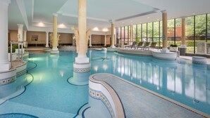 Une piscine intérieure dotée de plusieurs couloirs, de grandes colonnes et de larges fenêtres laissant entrer la lumière du soleil.