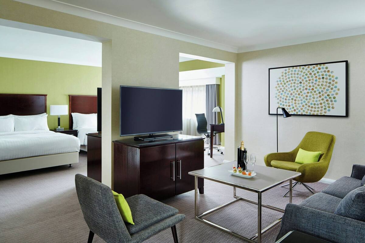 A hotel room with a bed, a television, a desk with a chair, a sofa, and a decorative wall piece.