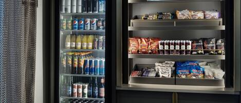 Máquina expendedora llena de bebidas y aperitivos, incluyendo refrescos, bebidas energéticas y alimentos envasados.