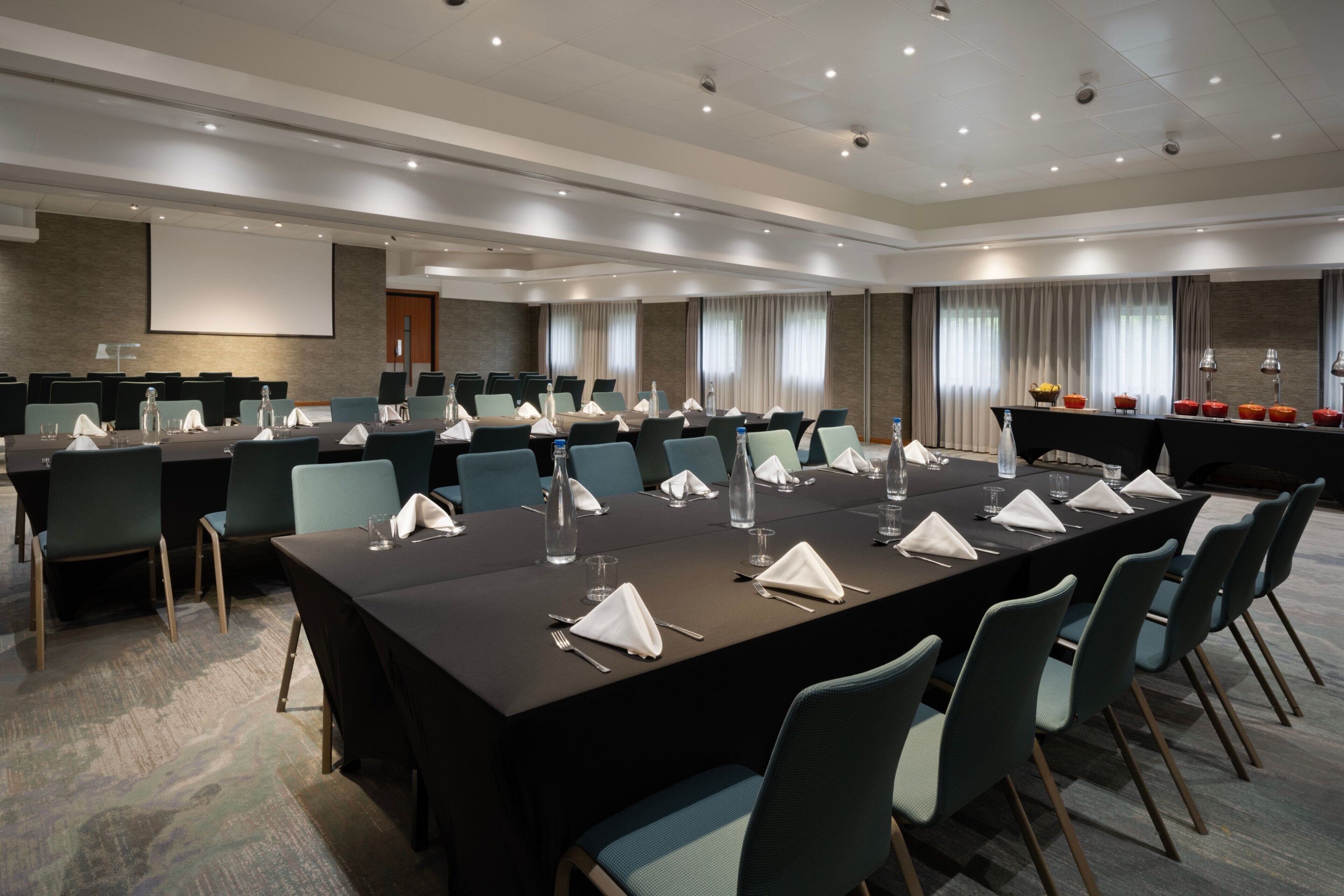 A conference room with a long table, multiple chairs, and a projector screen.