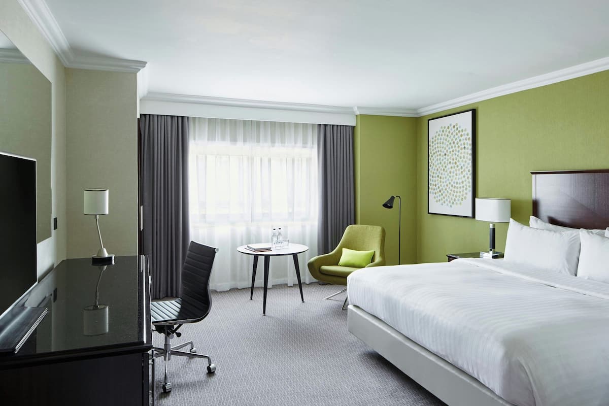 A hotel room with a bed, a desk with a chair, a small table, and a TV.