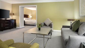 A modern hotel room with a flat-screen TV, a small table, a sofa, and a bed in the background.