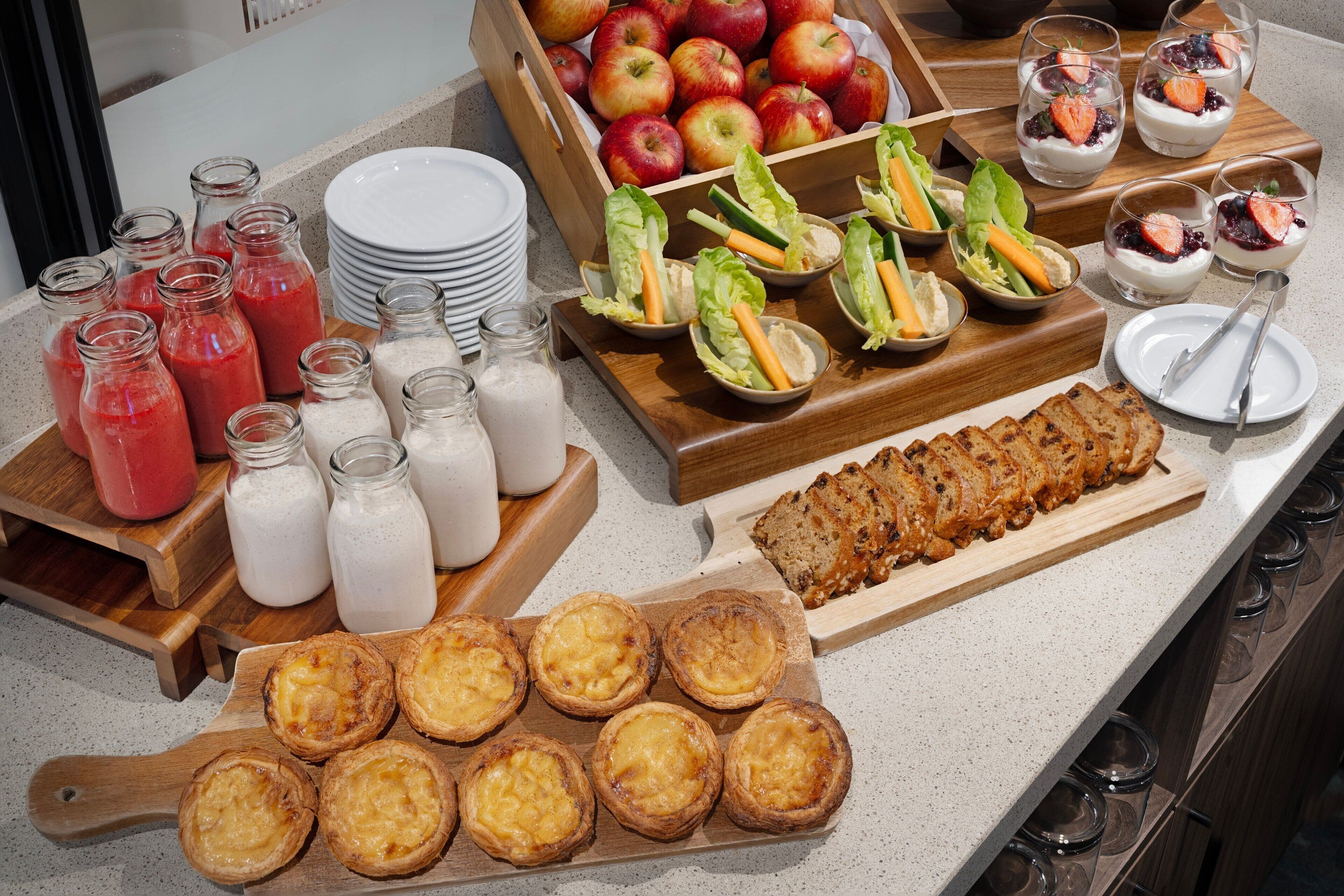 A buffet with various food items including apples, sandwiches, and pastries.