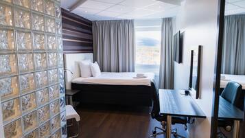 A modern hotel room with a large bed, a desk, a chair, and a view of the mountains.