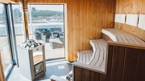A sauna room with wooden walls, a bench, and a stone heater. - Grand Hotel Lapland (Gällivare)