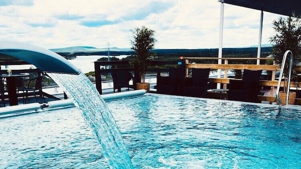 A swimming pool with a waterfall feature, surrounded by lounge chairs and a covered area. - Grand Hotel Lapland (Gällivare)