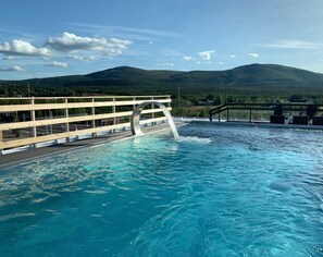 A swimming pool with a wooden deck and a view of a mountain range. - Grand Hotel Lapland (Gällivare)