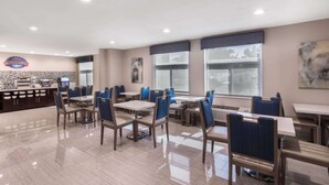 Ein sauberes, helles Restaurant mit mehreren Tischen und Stühlen, einer Theke mit einer Kaffeemaschine und großen Fenstern, die für natürliches Licht sorgen.