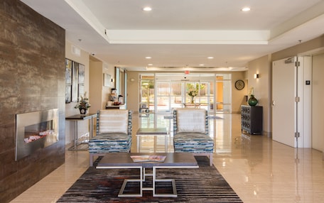 A spacious lobby with a modern design, featuring a reception desk, seating area with patterned chairs, and a decorative wall.