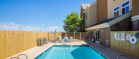 A swimming pool with lounge chairs and a wooden fence.