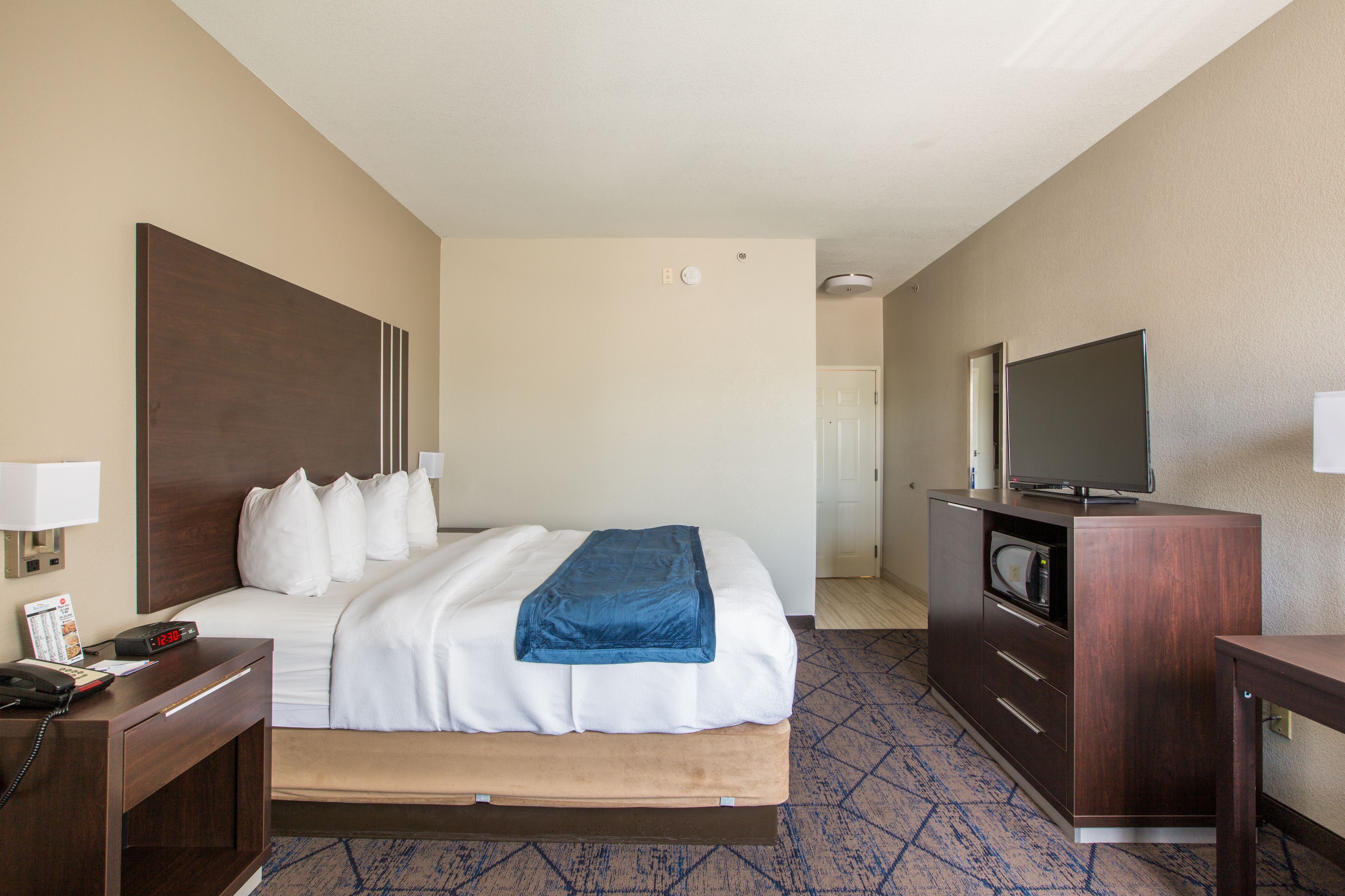 Une chambre d’hôtel comprenant un lit, un bureau avec un téléphone, un téléviseur posé sur un meuble et une commode.