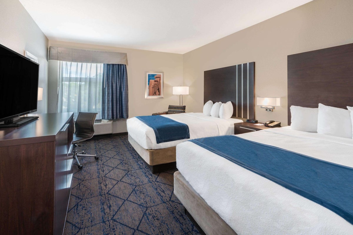Een hotelkamer met twee bedden, een bureau, een televisie en een groot raam met gordijnen.