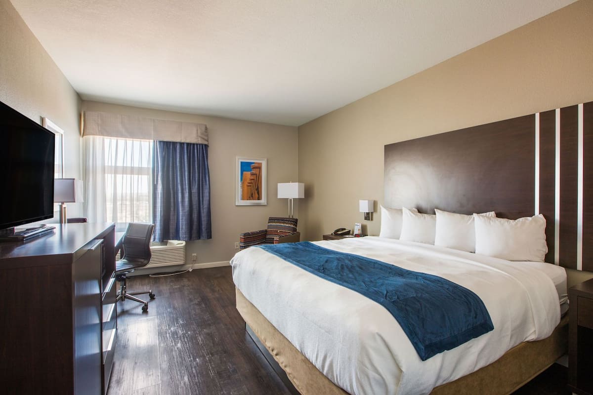 Een hotelkamer met een bed, bureau, televisie en uitzicht op de stad.