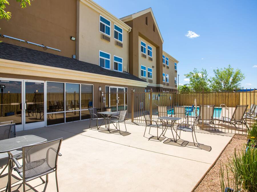 A poolside area with lounge chairs and tables, a pool, and a building with large windows and a wooden fence.