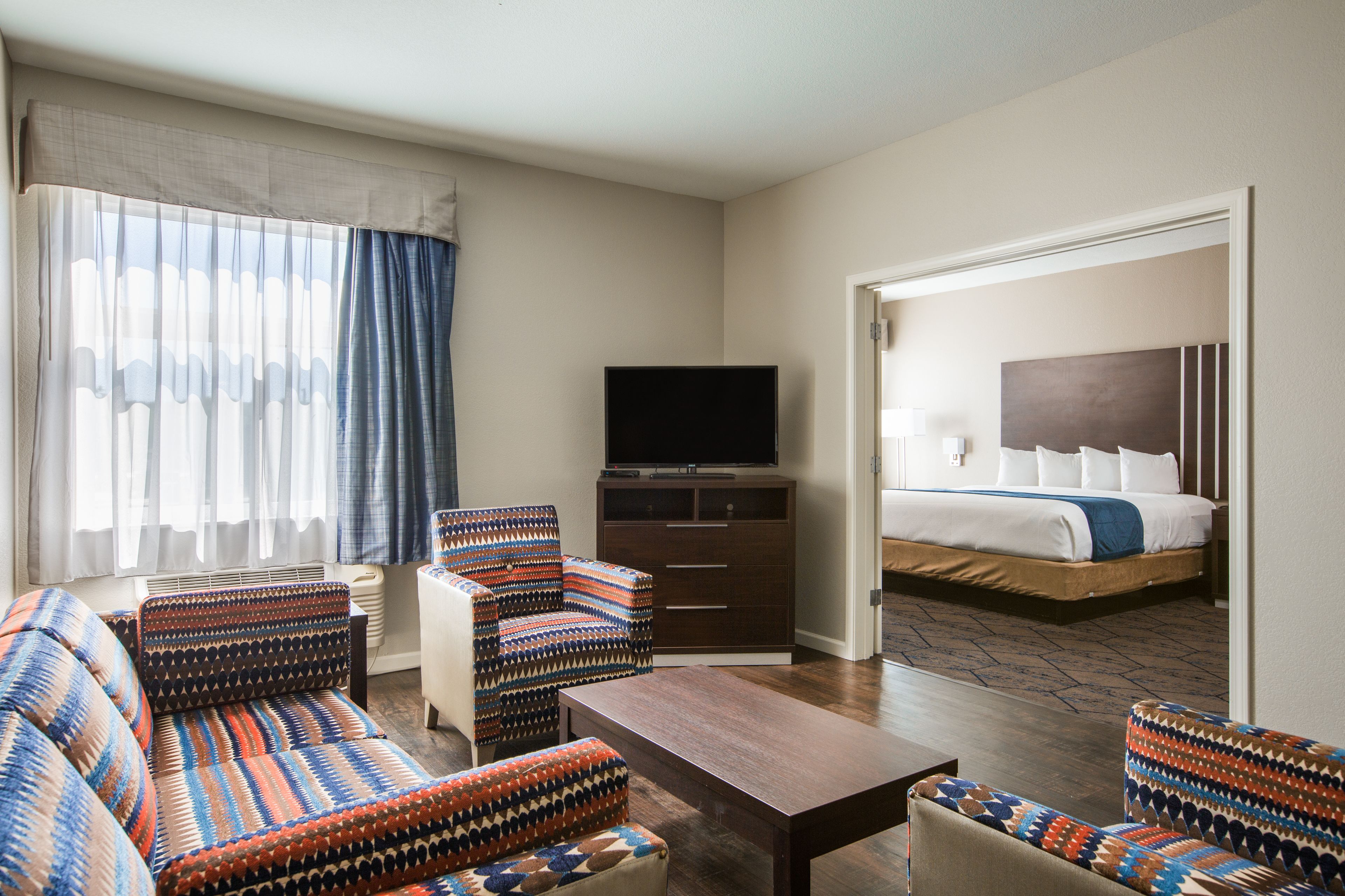 A hotel room with a sofa, armchair, TV, and a bed with a headboard.