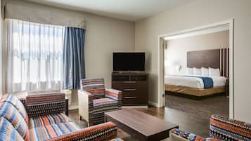 A hotel room with a sofa, armchair, TV, and a bed with a headboard.