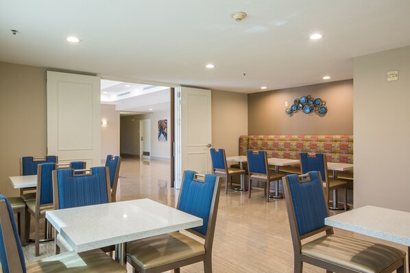 Un comedor de hotel con mesas y sillas, una pared con un diseño decorativo e iluminación empotrada en el techo.
