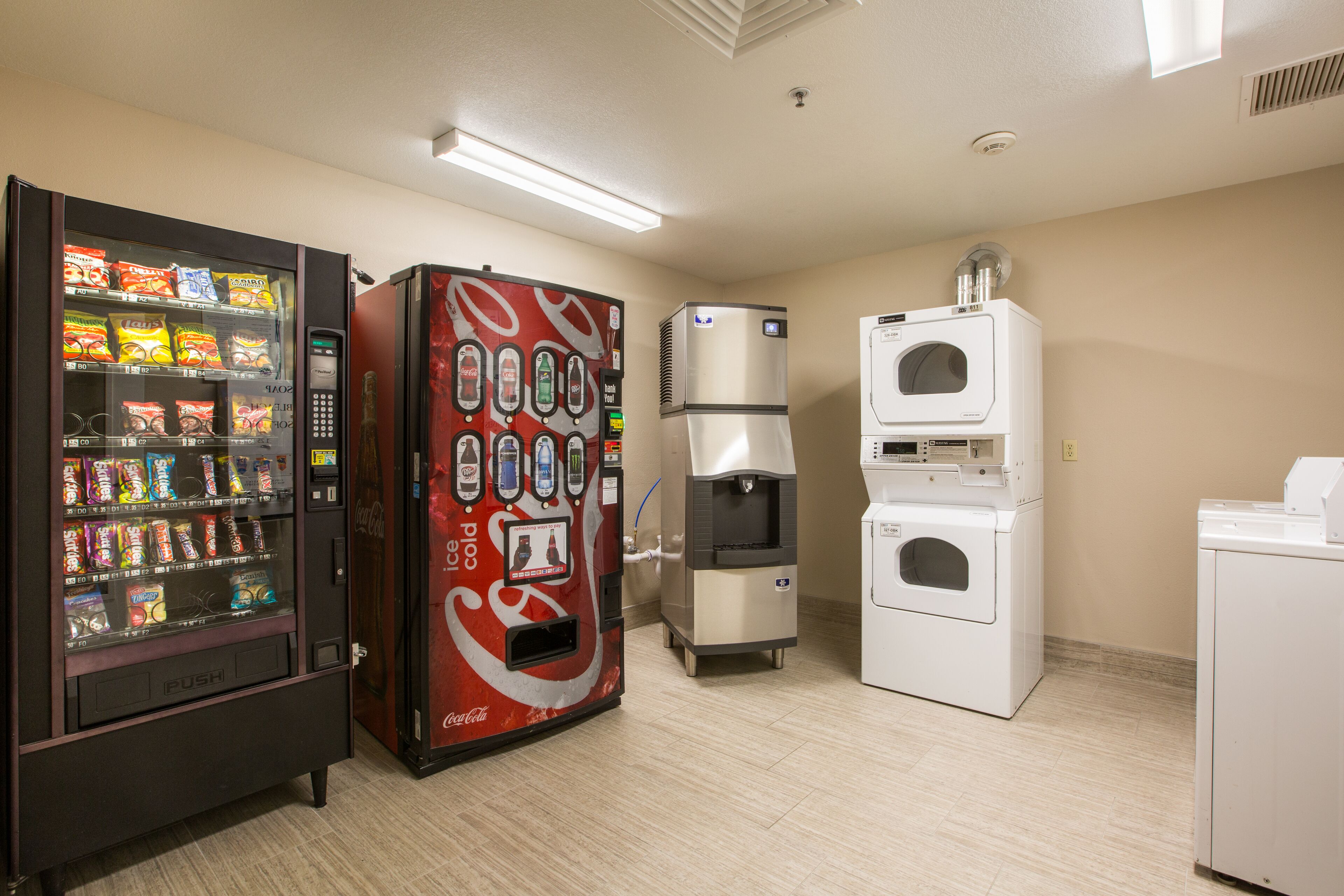 A vending machine area with a Coca-Cola cooler, a snack vending machine, and a washer-dryer unit.
