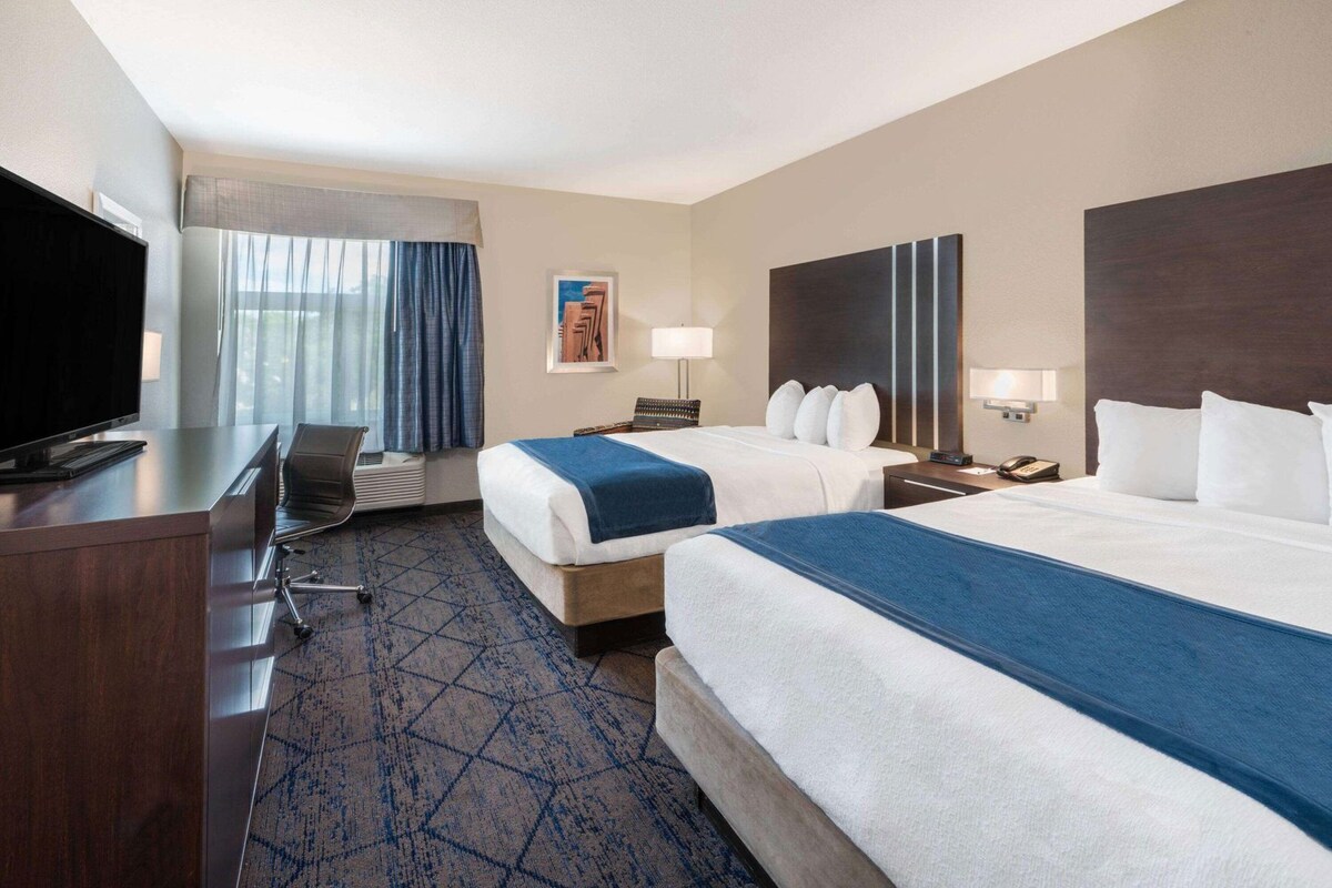 Une chambre d’hôtel avec deux lits, un bureau avec une télévision, une chaise, une lampe de bureau, un téléphone et un tableau au mur.