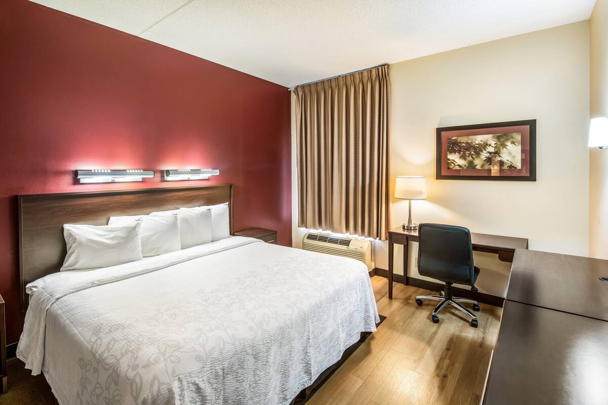 Habitación de hotel con una cama grande, un escritorio, una silla, una lámpara y un cuadro en la pared.